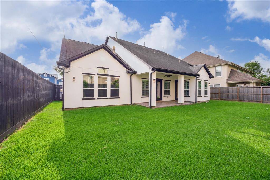 This backyard features a large grassy area and a covered patio, perfect for outdoor play or entertaining.