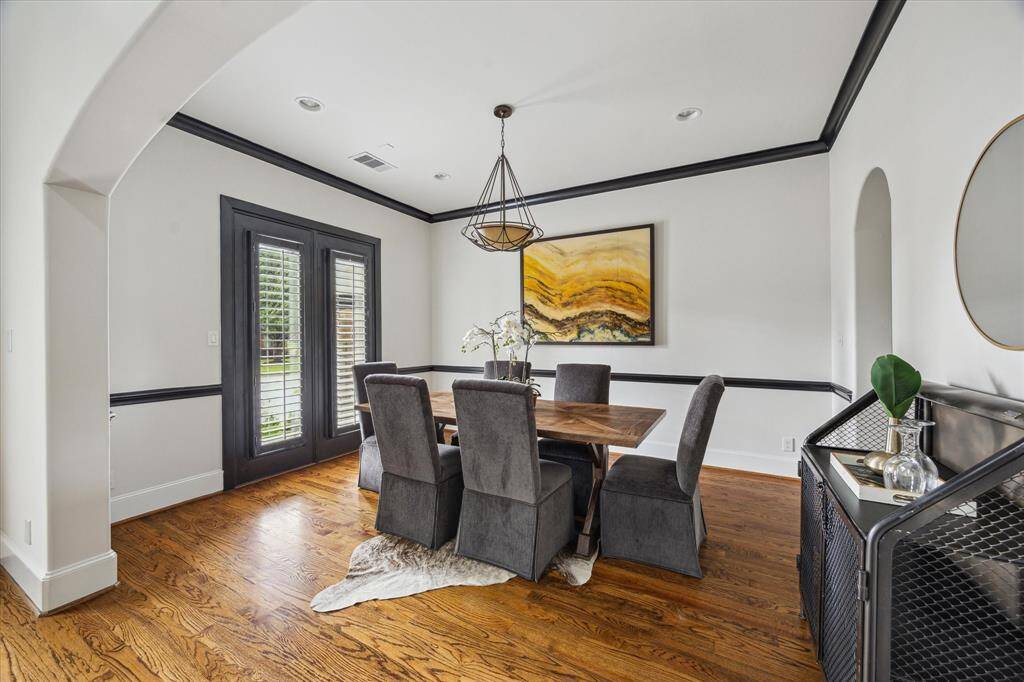 Formal dining room with rich wood floors, double doors for natural light, and bold black trim for a striking contrast.