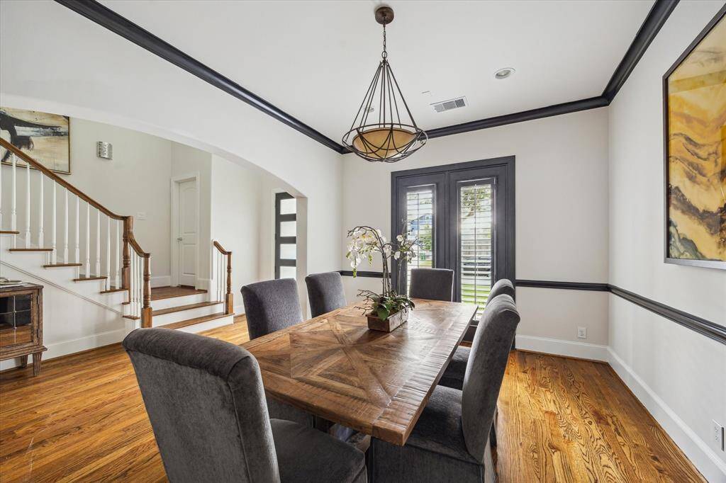 Formal dining room with hardwood floors, bold black trim, and direct access to the front entry through an arched opening. Natural light filters in through large shuttered doors.