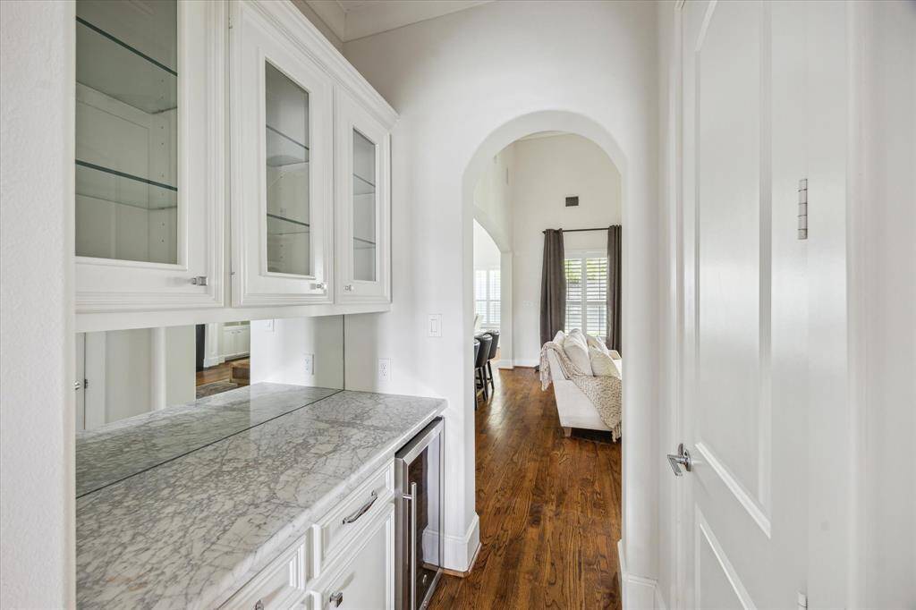 This butler’s pantry features marble countertops, upper glass-front cabinets, and a built-in beverage fridge, conveniently connecting the kitchen to the dining area.