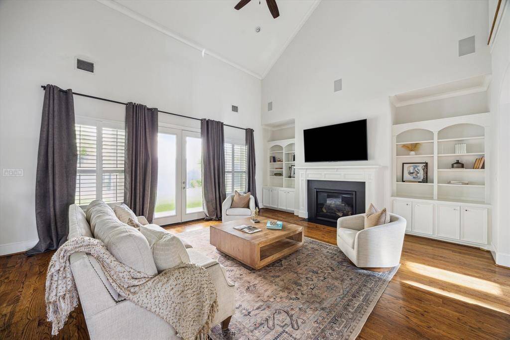 Spacious family room with vaulted ceilings, built-in shelving, a central fireplace, and French doors that open to the backyard.
