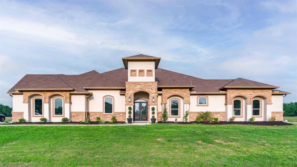 This photo showcases a spacious, modern ranch-style home with a symmetrical design. It features a mix of stucco and stone exterior, a central entrance with arched windows, and well-maintained landscaping on a large, open lawn.