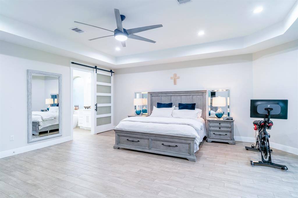 This spacious Primary Bedroom features a modern design with tile wood flooring and recessed lighting. It has 2 walk in closets and a sliding barn door leading to an ensuite bathroom offering both comfort and functionality.
