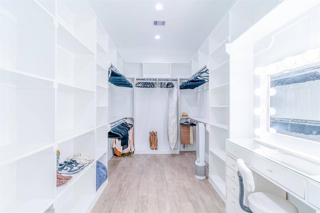 This spacious walk-in closet features ample shelving, hanging space, and a chic vanity area with illuminated mirror, all set on elegant wood flooring. Ideal for organizing clothes and accessories stylishly.