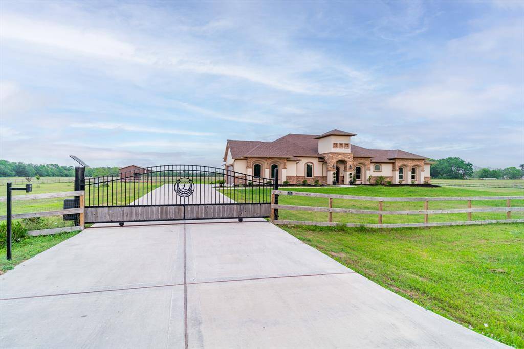 Spacious and secluded property featuring a modern ranch-style home with a large, well-maintained lawn. The gated entrance provides security and privacy, while the surrounding open fields offer a serene, countryside atmosphere.