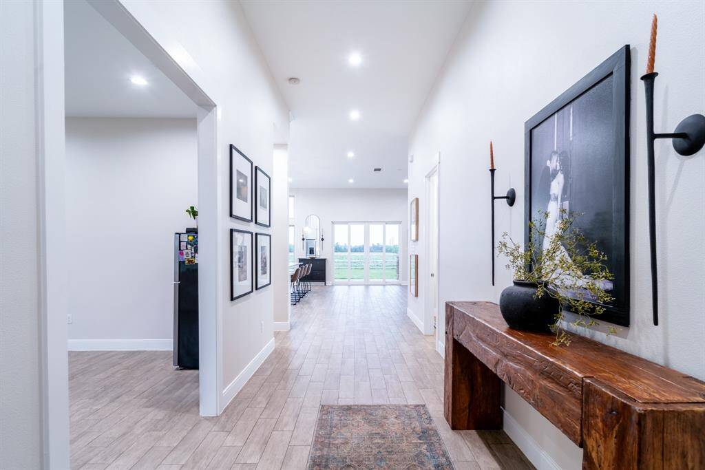 Bright, welcoming hallway with tile wood flooring and modern decor. Features a view into an open kitchen with bar seating and large windows showcasing greenery.