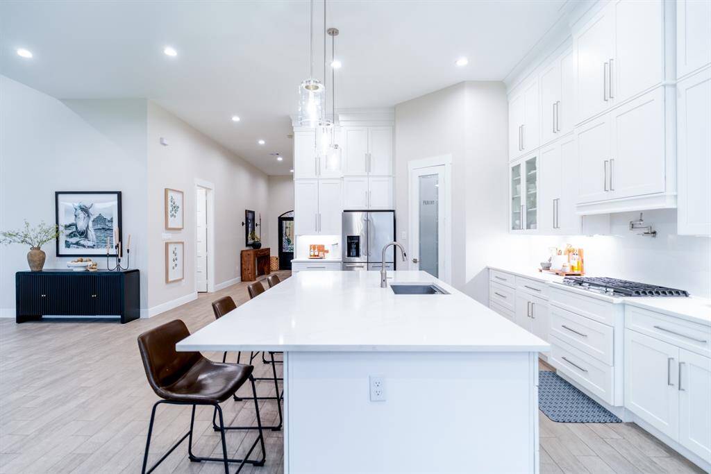 Bright, modern kitchen with sleek white cabinetry, a large island with seating, and stainless steel appliances. Open layout with high ceilings and stylish decor, perfect for entertaining.