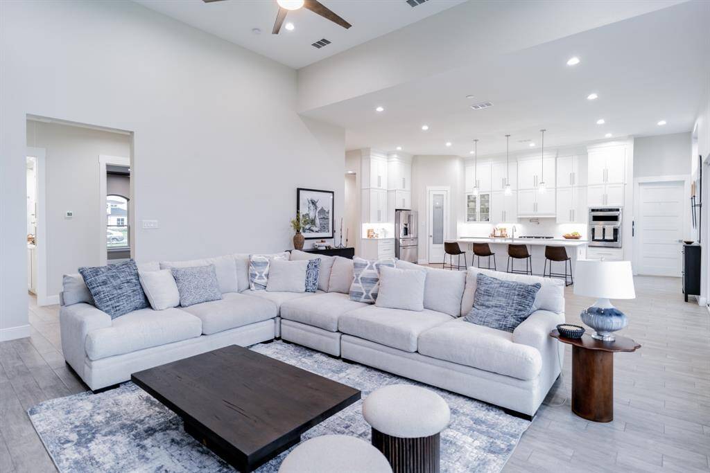 This spacious open-concept living area features a modern kitchen with white cabinetry, a central island with bar seating, and stainless steel appliances. The living room has a large sectional sofa, stylish decor, and a cozy atmosphere, perfect for entertaining or relaxing.