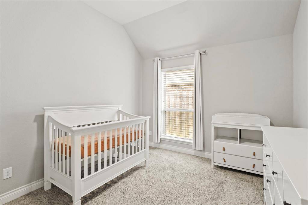 A cozy, neutral-toned room which features soft carpet flooring and a window with white blinds, letting in natural light.