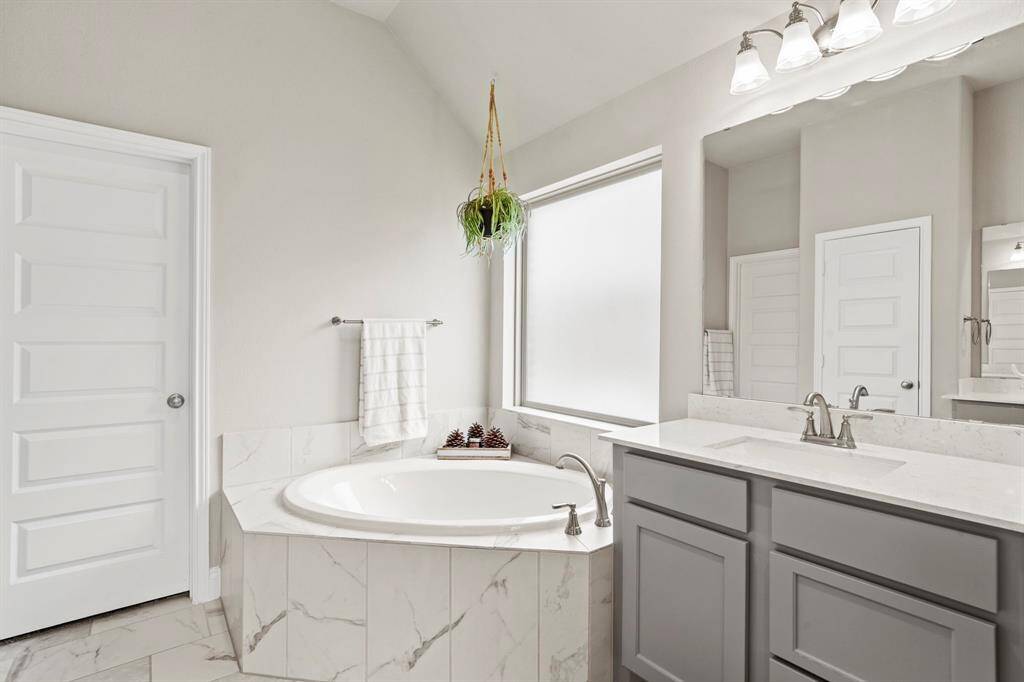 A close-up view of the soaking tub under a large frosted window, flanked by a sleek vanity with under-mount sink and contemporary fixtures. A hanging plant adds a soft natural touch.
