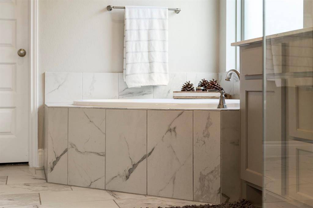 Elegant soaking tub surrounded by marble tile with a chrome faucet, adjacent to a dual vanity.