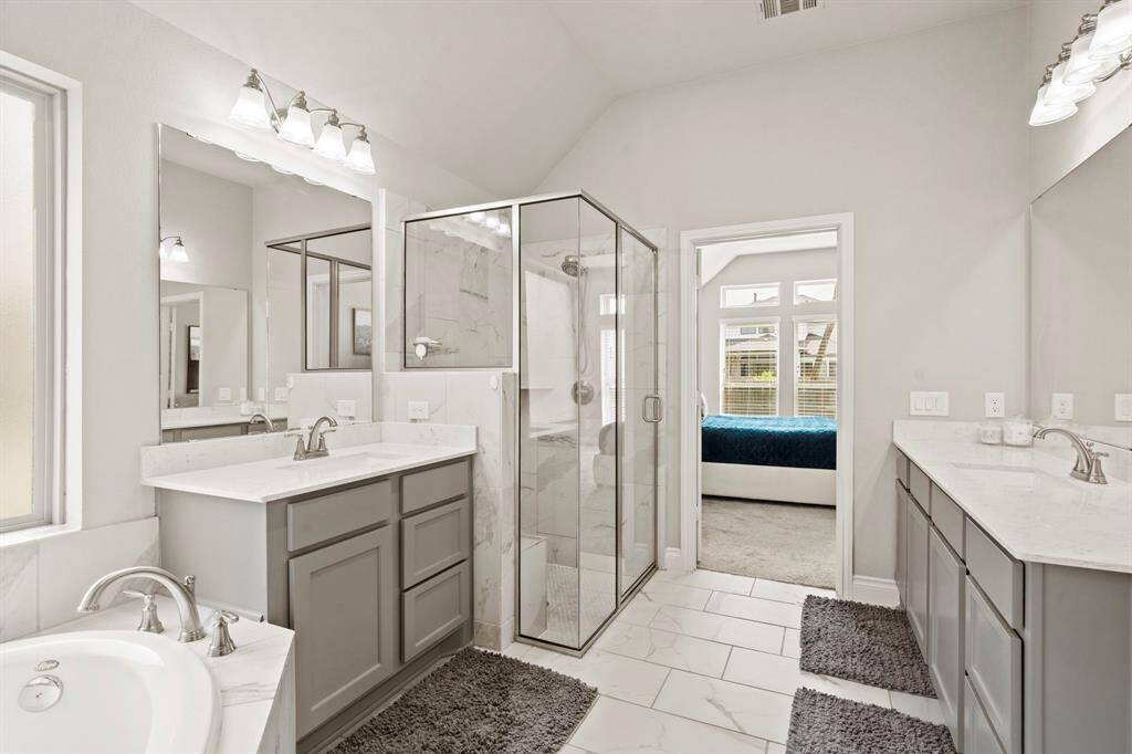 This view shows the bathroom layout with dual vanities and a walk-through into the primary bedroom. Soft lighting and neutral finishes create a spa-like feel.