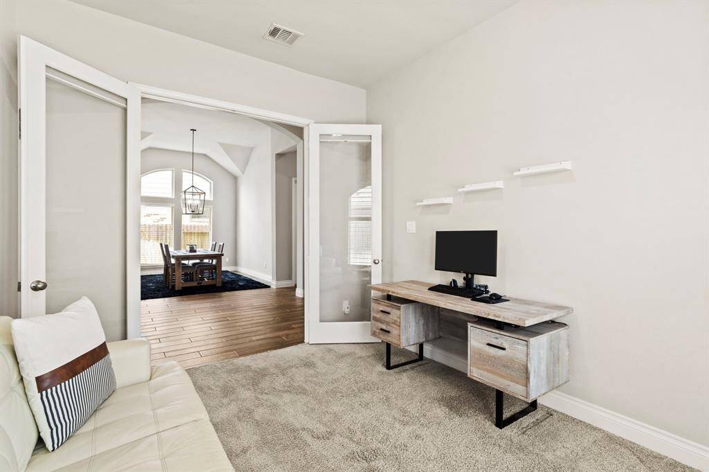 A cozy office or study space with glass French doors opening to a dining area with vaulted ceilings and large windows.