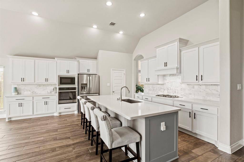 A modern kitchen featuring a large island with seating, stainless steel appliances, white cabinetry, and elegant marble backsplash.
