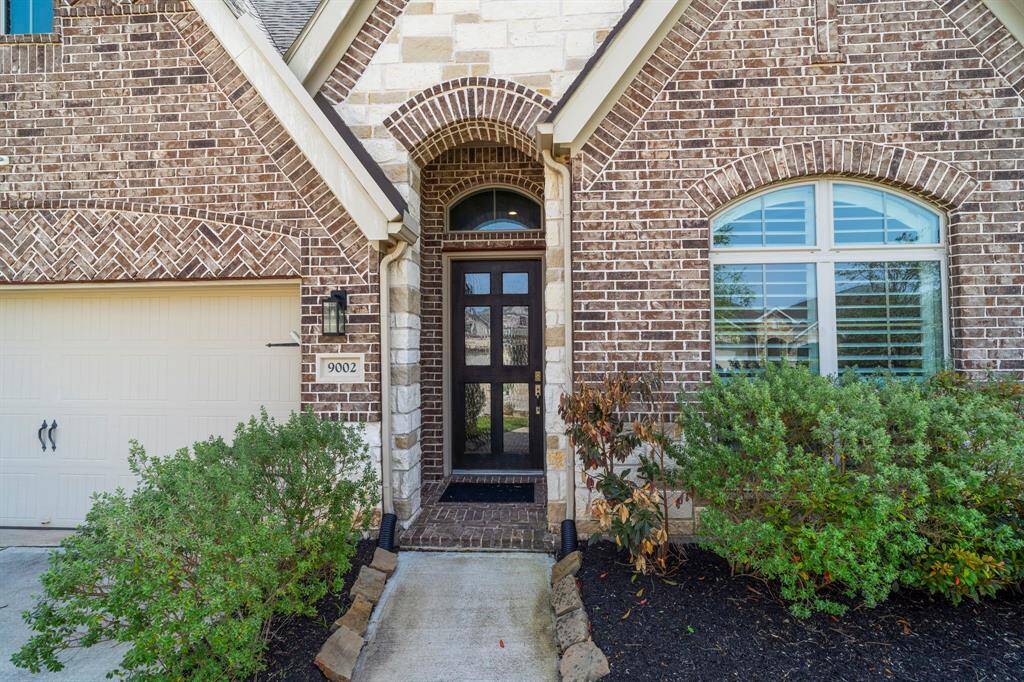 Inviting front entry with dark wood door, arched brick detail, and neatly landscaped flower beds.