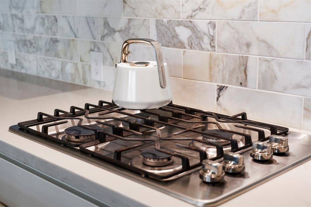 Close-up of the stainless steel gas cooktop, set against an elegant marble tile backsplash.