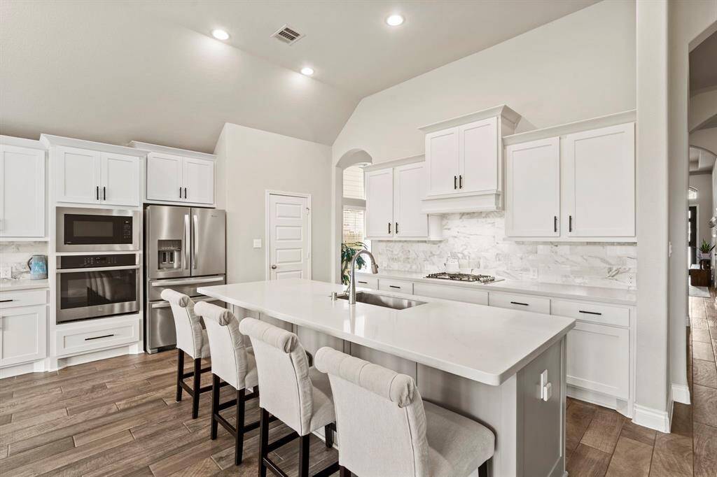Spacious and modern kitchen with white cabinetry, marble backsplash, stainless steel appliances, and an oversized island with seating for four.