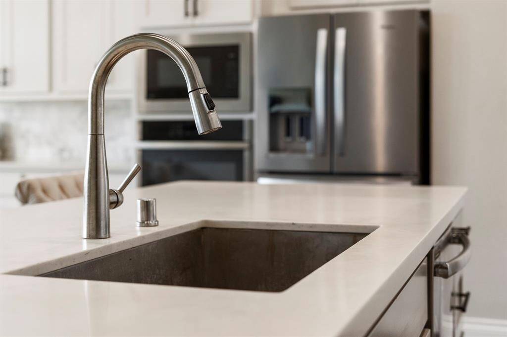 Modern pull-down faucet over a stainless steel under-mount sink, with a clean quartz countertop and appliances in the background.