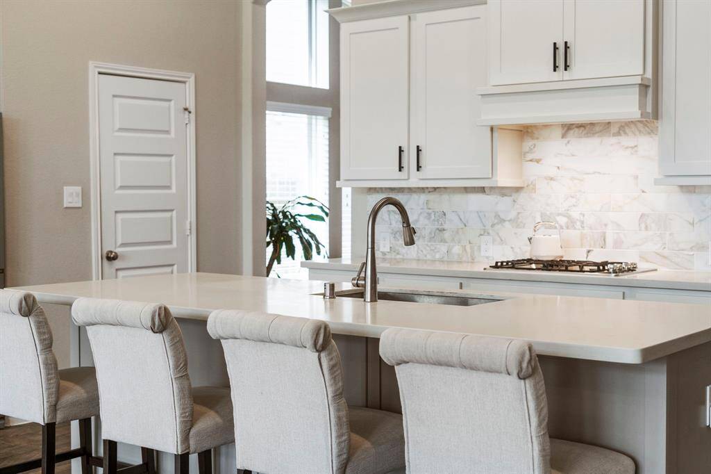 View of the island with detailed focus on the marble tile backsplash and additional seating.