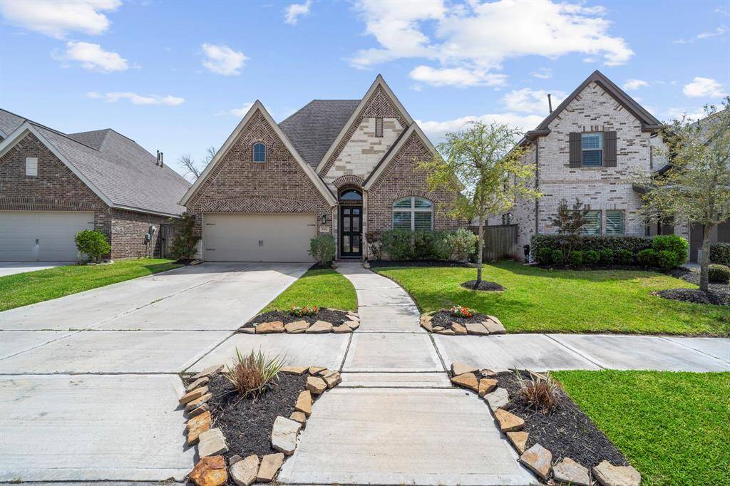 A slightly closer view of the same home, showing more detail of the brickwork and stone accents. The lush green lawn and small flower beds provide a welcoming feel.