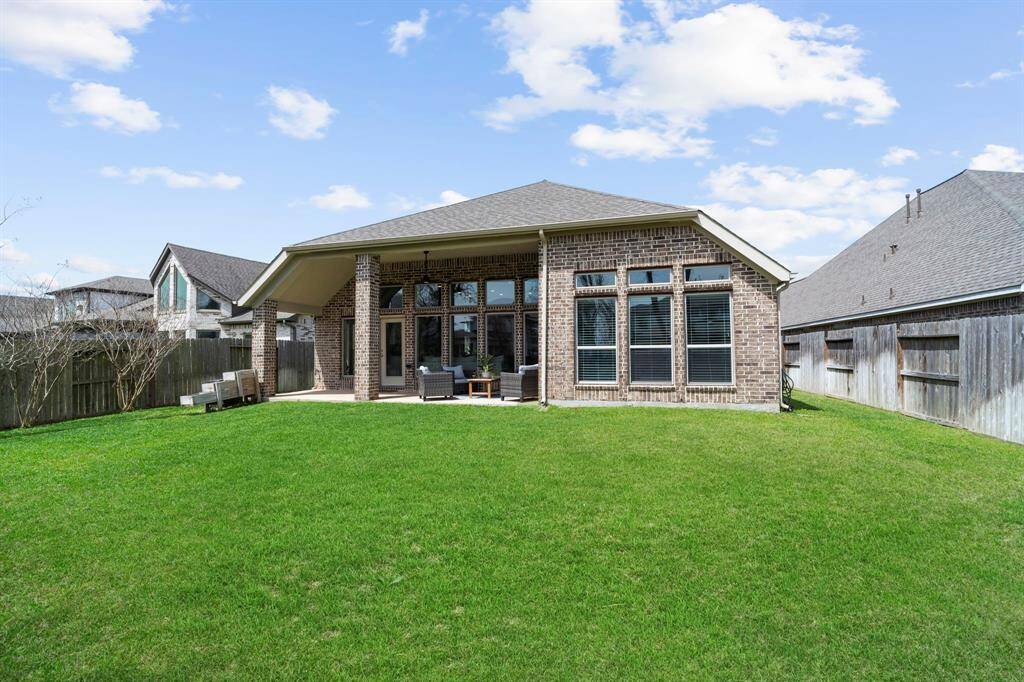 Full view of the backyard and the rear facade of the home, showcasing the spacious lawn and covered patio.