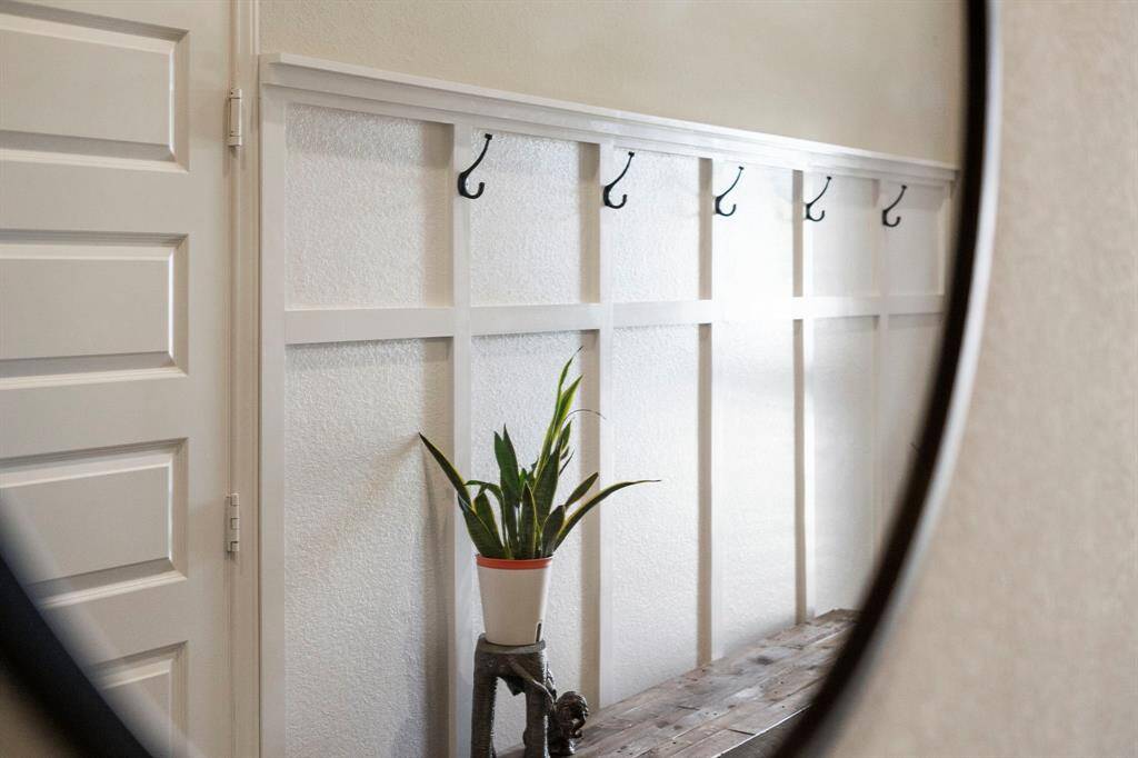 A stylish hallway nook with board and batten wall treatment, black hooks, and a rustic bench, reflected in a decorative mirror.