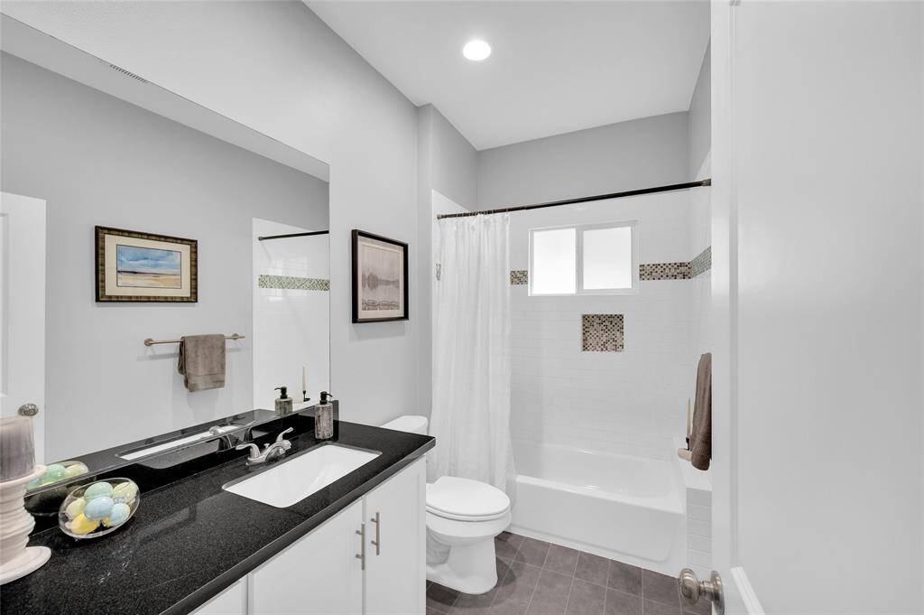 The full bath with black granite counter and white tiled tub and shower.