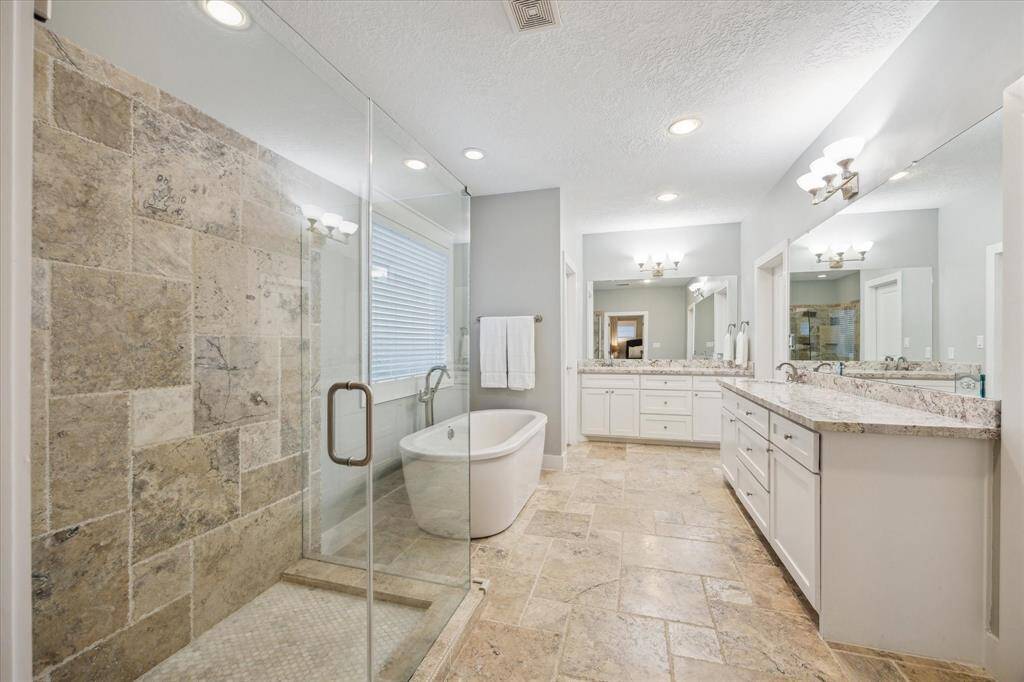 PRIMARY BATH - Spa-like bathroom with stone tile, granite countertops, double vanities, freestanding tub and walk-in shower with frameless glass surround.