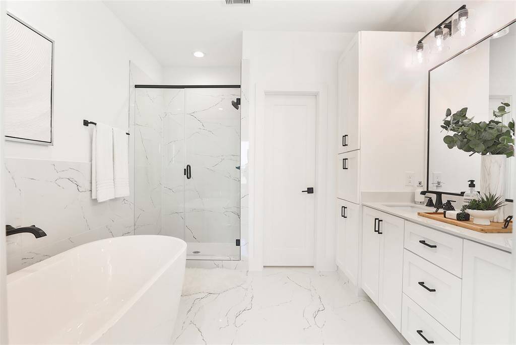 Luxurious porcelain floor tiles and glossy white subway tiles create an elegant atmosphere. Windows above the soaking tub provide natural light while ensuring privacy, and the black wall-mounted faucet enhances the modern aesthetic.