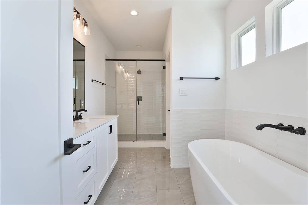 12"x3" glossy white subway picket tiles complement the windows above the luxurious soaking tub, creating a bright and elegant retreat.