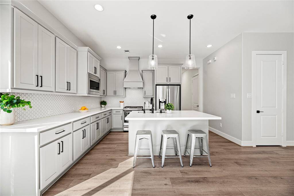 Features include quartz countertops paired with a coordinating backsplash, stainless steel appliances, crisp white cabinets with updated hardware, recessed and pendant lighting, and a sprawling island with breakfast bar seating.