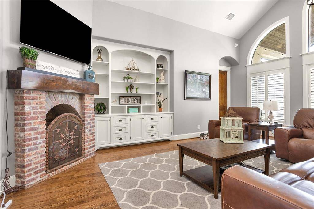 A spacious and elegant living area featuring soaring ceilings, rich wood flooring, a cozy gaslog fireplace, and large windows that bring in natural light—perfect for entertaining or relaxing in style.