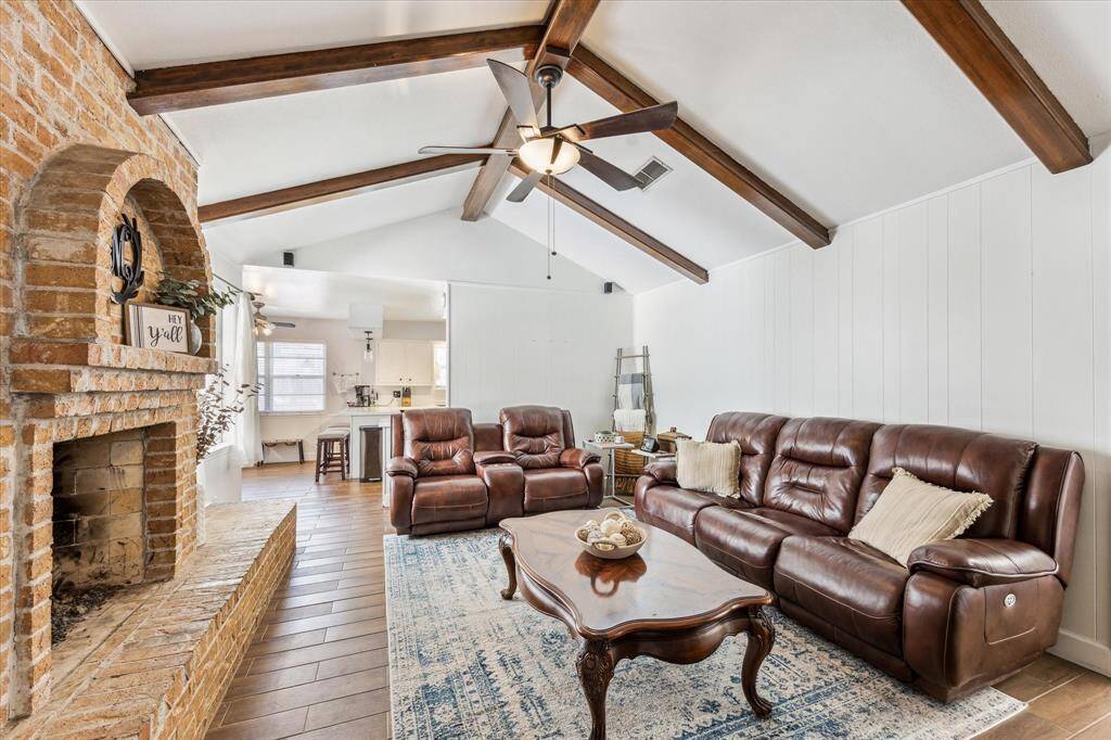 The living room showcases stunning vaulted ceilings with wooden beams and opens up to the breakfast room and kitchen.