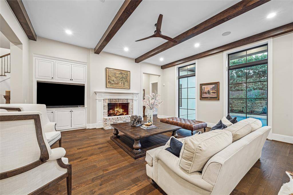 A cozy yet spacious gathering area, the family room features a striking brick fireplace, wood beams on the ceiling, and custom built-ins designed to accommodate a large television. In-ceiling speakers add the perfect touch for entertainment. The primary bedroom is conveniently located nearby on the left side of the house, just off the family room.