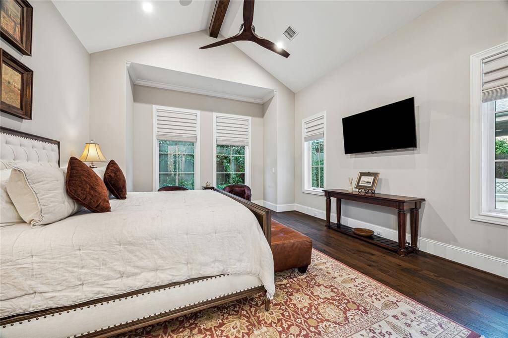 The serene primary suite features cathedral ceilings with a wood center beam and fan, rich hardwood floors, and large windows adorned with Hunter Douglas shades that frame stunning views of the pool. The luxurious ensuite bath completes the retreat-like experience.