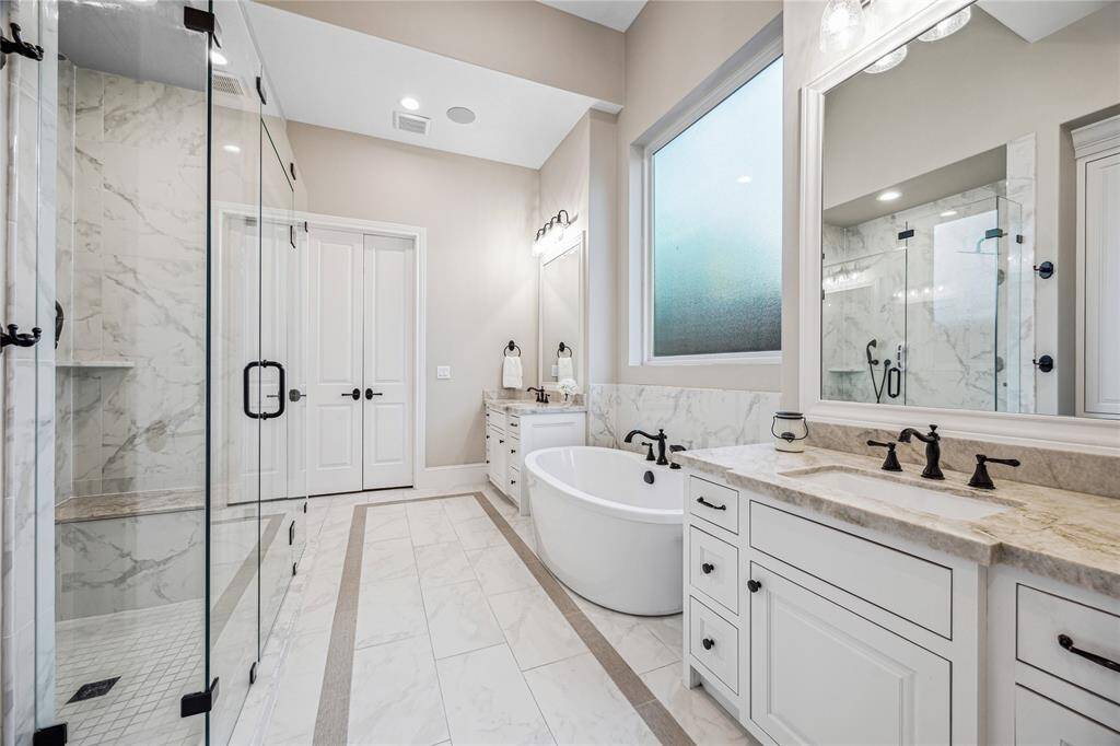 A freestanding soaking tub with a handheld sprayer and a large privacy glass window provide a spa-like atmosphere.