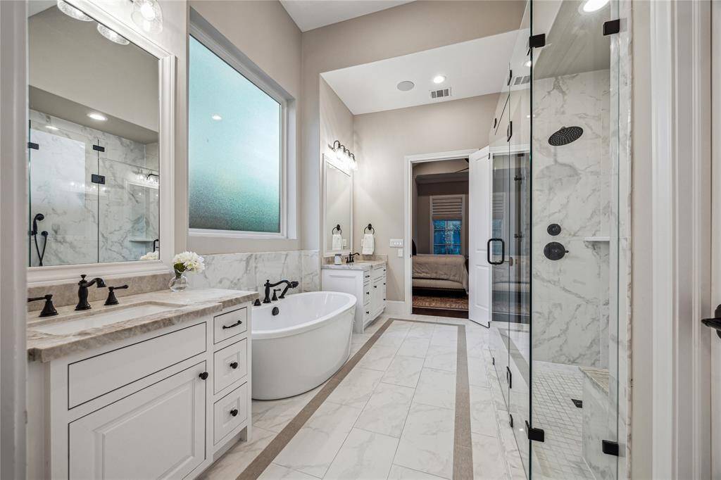 A luxurious oasis, the primary bathroom features custom inset vanities with quartzite countertops and built-in hampers in the linen closet.