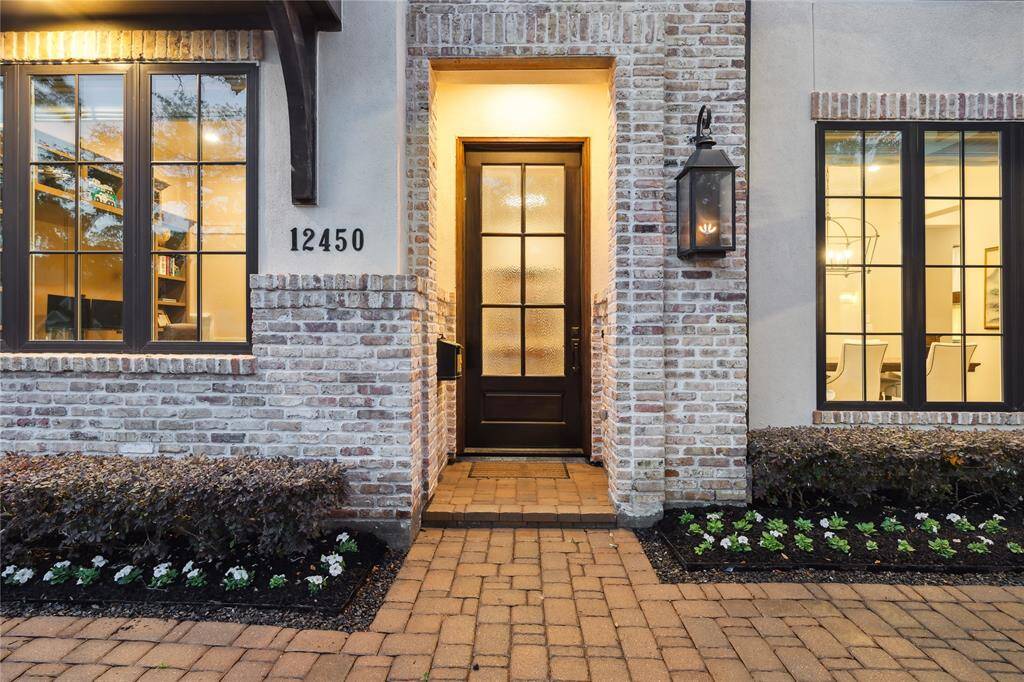 Welcoming entryway with a custom 8' solid wood door and charming gas lanterns, framed by a brick-paver driveway.