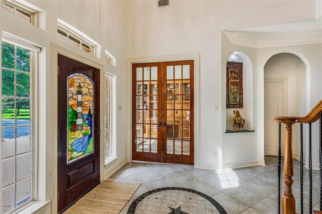 This foyer features a stunning stained glass front door, ample natural light from side windows, and elegant tile flooring.