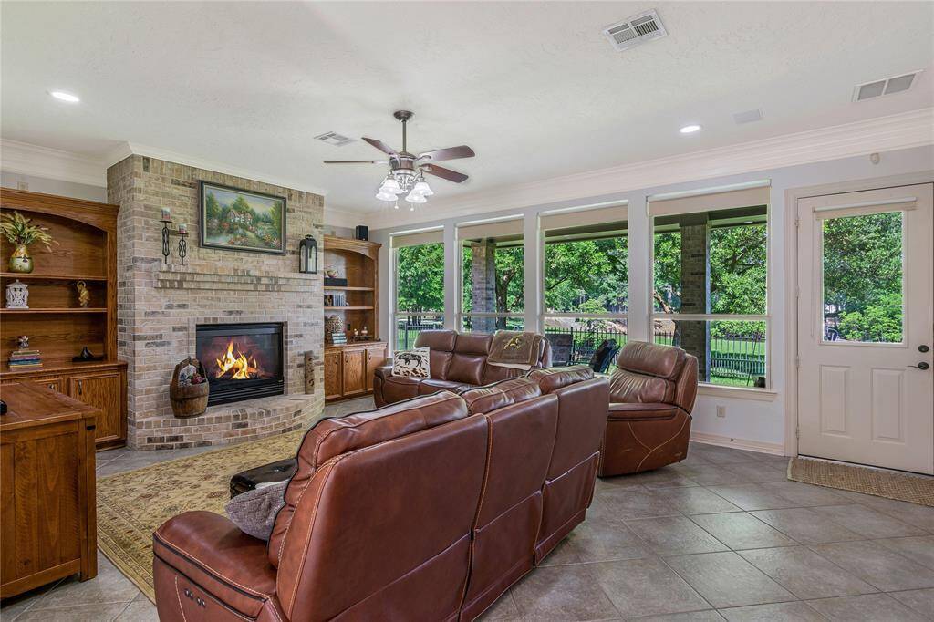 This cozy living room features a brick fireplace, built-in wooden shelves, and large windows offering a scenic view of lush greenery.
