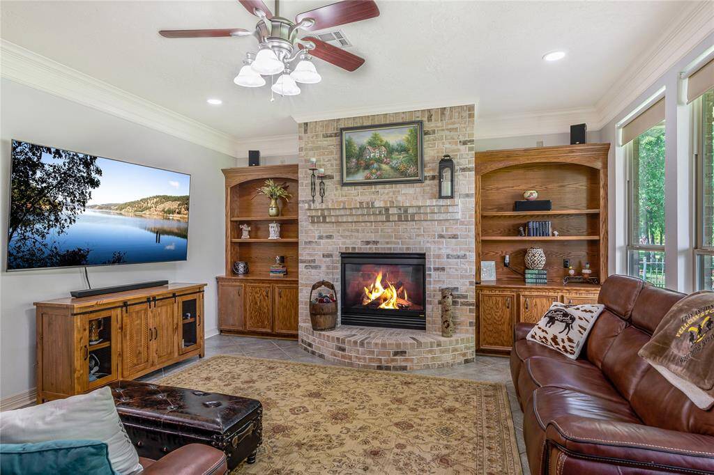 This cozy living room features a brick fireplace with built-in wooden shelves on either side. The room is well-lit with natural light from the windows and a ceiling fan for comfort.