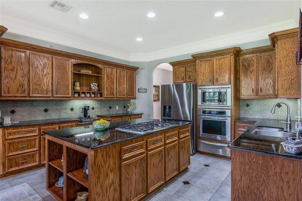 This kitchen features rich wooden cabinetry, granite countertops, and a central island with a cooktop. Stainless steel appliances and ample storage offer functionality, while recessed lighting adds a modern touch.