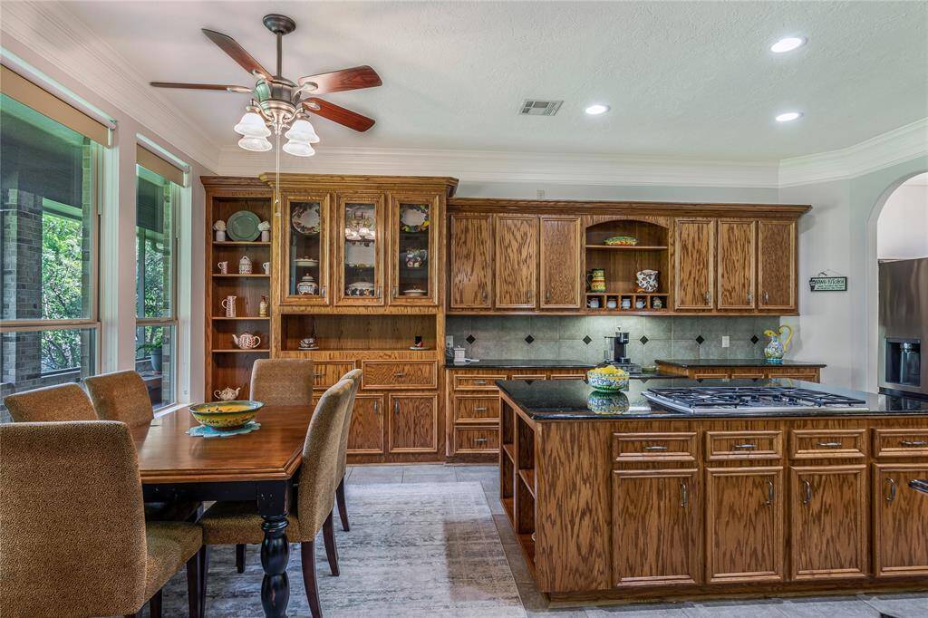 This kitchen features rich wood cabinetry with ample storage, a central island with a gas cooktop, and granite countertops. The dining area is adjacent, with large windows for natural light.