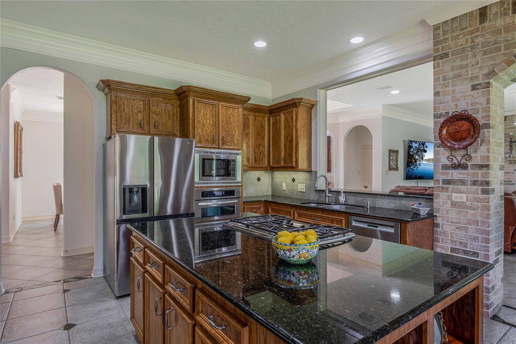 This kitchen features elegant wood cabinetry, stainless steel appliances, and a spacious island with a gas cooktop. The open layout connects to the living area, creating a seamless flow for entertaining. Modern lighting and a tiled floor enhance the stylish and functional design.