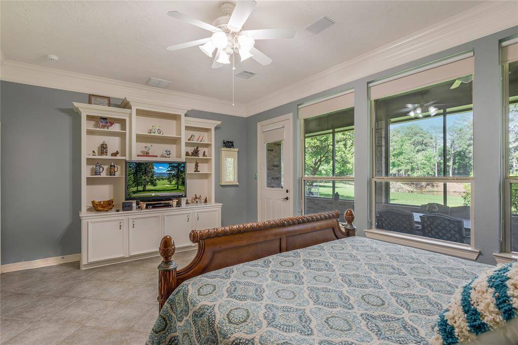 This photo showcases the cozy primary bedroom with soft blue walls, a ceiling fan for comfort, and tiled floors. Adjacent to the bedroom is the primary bathroom.