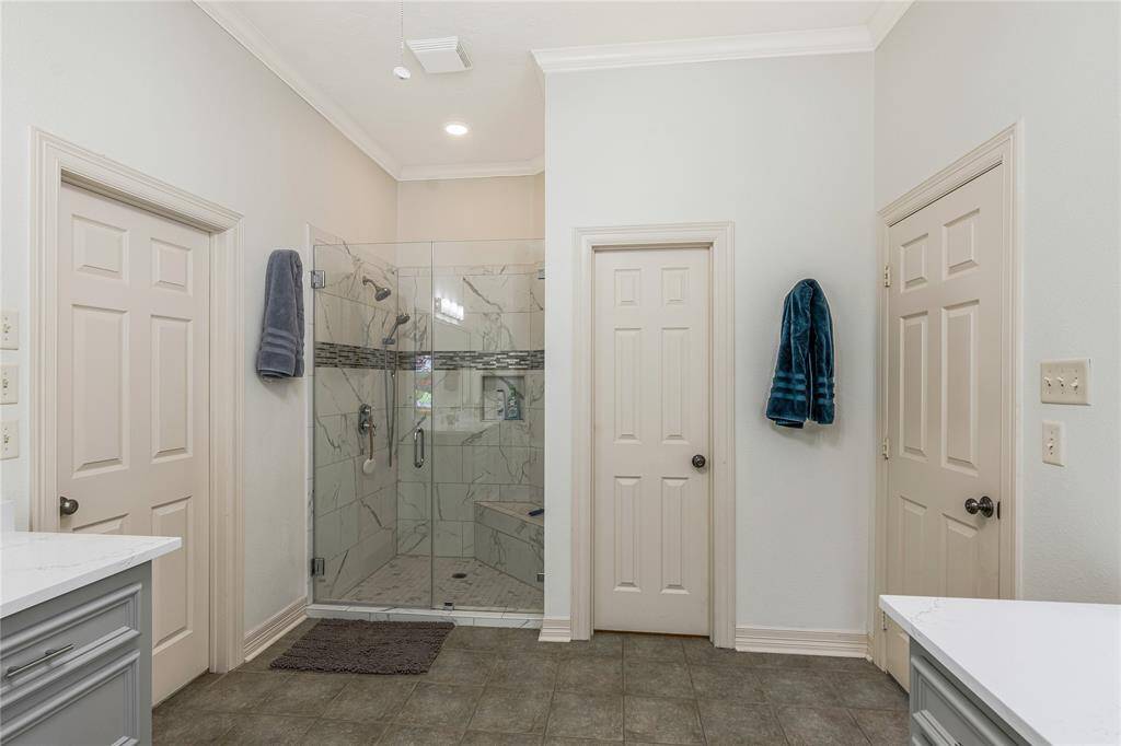 The spacious primary bathroom features a large glass-enclosed walk-in shower with elegant tile work. It includes two doors with ample storage space and modern fixtures.