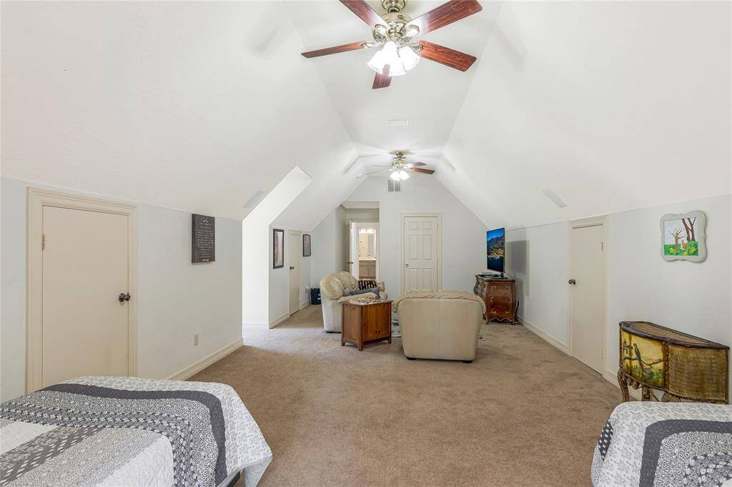 This spacious room features a cozy seating area, twin beds, and soft carpeting. With sloped ceilings and ceiling fans, it's an inviting multi-purpose space with ample natural light.