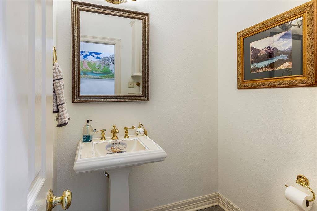 Cozy powder room with a pedestal sink, elegant gold fixtures, and a decorative mirror.