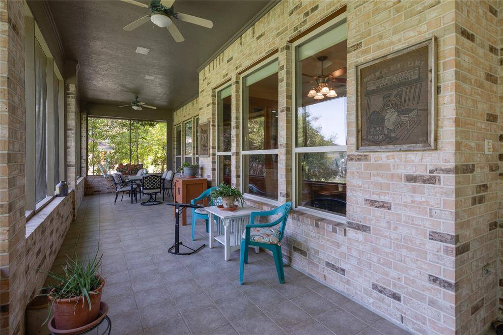 This photo showcases a spacious, screened-in porch with tiled flooring and brick walls. It features ceiling fans for comfort, large windows offering plenty of natural light, and multiple seating areas ideal for relaxation and entertaining. Lush greenery is visible outside, enhancing the serene ambiance.