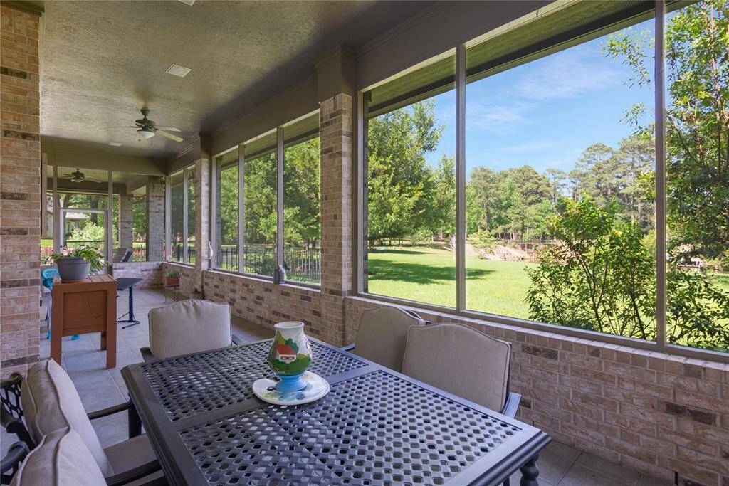 This photo showcases a spacious screened-in patio with brick walls, offering a serene view of a lush, green backyard. It's perfect for relaxing or entertaining, featuring comfortable seating and ceiling fans for added comfort.